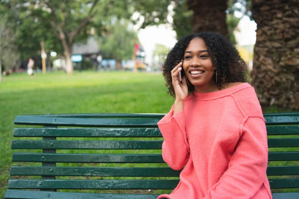 Güzel Afro-Amerikan bir kadının portresi telefonda konuşuyor ve parkta bir bankta oturuyor. Açık havada..