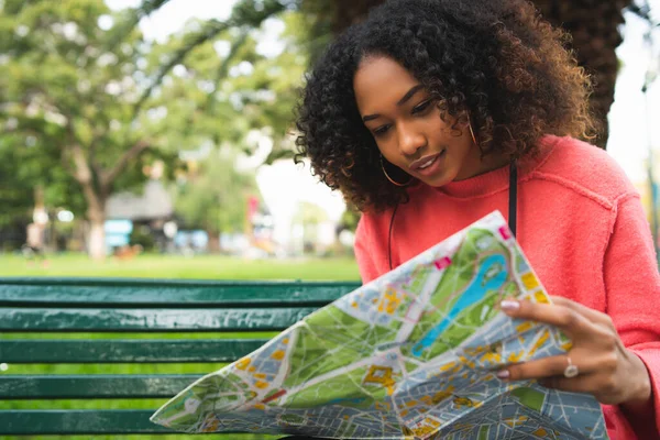 Parktaki bankta oturmuş haritaya bakan güzel Afro-Amerikan bir kadının portresi. Seyahat konsepti. Açık havada..