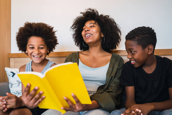 Portrait of Afro American mother reading a book to her children at home. Family and lifestyle concept.