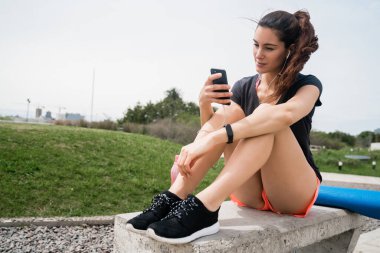 Eğitime ara verdiğinde cep telefonunu kullanan atletik bir kadının portresi. Spor ve sağlık yaşam tarzı.