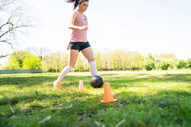 Genç bayan futbolcunun portresi sahada top oynarken koni etrafında koşuyor. Spor konsepti.