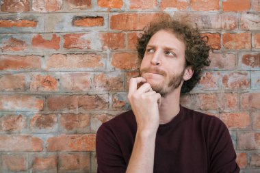 Caddedeki tuğla duvara karşı düşünceli bir ifadeyle genç beyaz adamın portresi. Şehir konsepti.