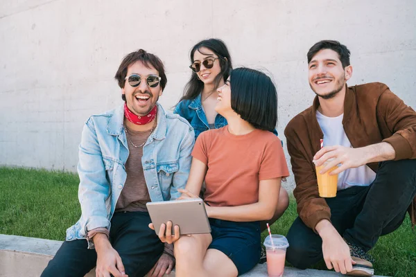 Bir grup arkadaşın dışarıda otururken birlikte eğlendikleri ve dijital tablet kullandıkları portre. Teknoloji, yaşam tarzı ve arkadaşlık kavramı.