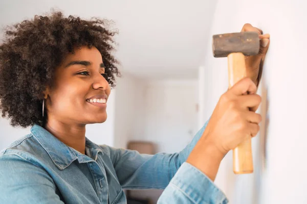 自宅の壁に釘を打つ若いアフロ女性の肖像画 ホーム改善と修理ホームコンセプト — ストック写真