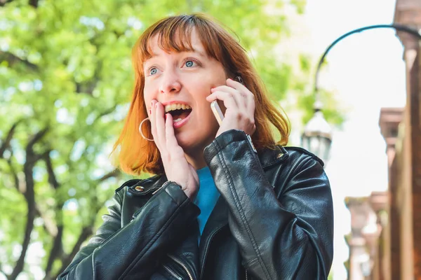 Portrait of young redhead woman talking on the phone outdoors in the street. Urban concept.