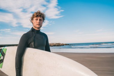 Genç sörfçü siyah sörf takımıyla okyanusta duruyor. Spor ve su sporları konsepti.