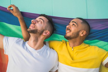 Sokakta gökkuşağı bayrağıyla sarılıp sevgilerini gösteren genç eşcinsel çiftin portresi. LGBT ve aşk konsepti