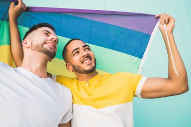 Sokakta gökkuşağı bayrağıyla sarılıp sevgilerini gösteren genç eşcinsel çiftin portresi. LGBT ve aşk konsepti