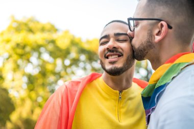 Genç eşcinsel çiftin portresi. Sokakta gökkuşağı bayrağıyla kucaklaşıp sevgilerini gösteriyorlar. LGBT ve aşk konsepti
