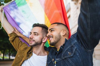 Sokakta gökkuşağı bayrağıyla kucaklaşan ve sevgilerini gösteren genç eşcinsel çiftin portresi. LGBT ve aşk konsepti