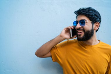 Telefonda mavi arka planda konuşan genç Latin adamın portresi. İletişim konsepti.