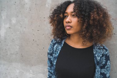 Gri duvarda kıvırcık saçları olan güzel Afro-Amerikan kadının portresi..