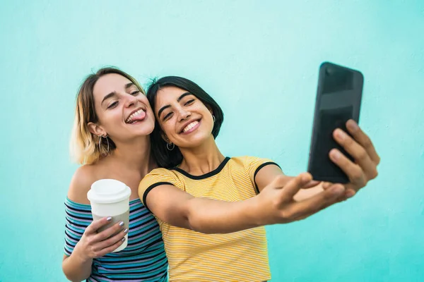 美しいレズビアンのカップルの肖像画は 楽しさを持っているとライトブルーの背景に携帯電話で自撮りします Lgbtの概念 — ストック写真