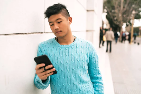 Sokakta cep telefonunu kullanan genç Asyalı adamın portresi. İletişim konsepti.