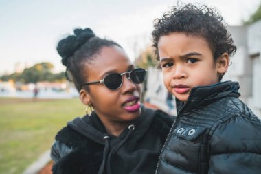 Afrika kökenli Amerikalı bir annenin portresi. Oğluyla parkta durmuş, eğleniyor. Monopental Ailesi.