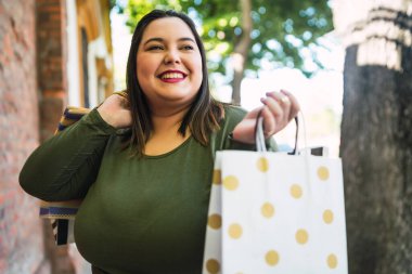 Sokakta alışveriş torbalarını tutan iri yarı genç bir kadının portresi. Alışveriş ve satış konsepti.