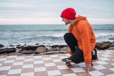 Kaykayıyla eğlenen genç bir adamın portresi ve arka planda deniz ile yaptığı numaralar..