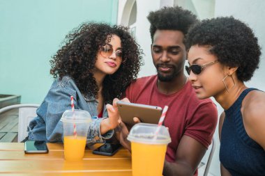 Üç afro arkadaşın birlikte eğlendikleri ve kafeteryada dijital tablet kullandıkları portre. Teknoloji konsepti.