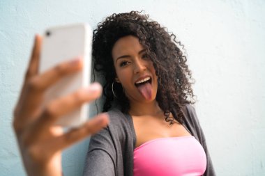 Mofili telefonuyla gri duvara selfie çeken afro kadın portresi. Teknoloji konsepti.