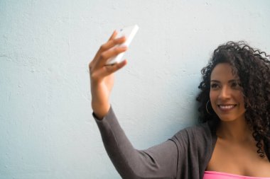 Mofili telefonuyla gri duvara selfie çeken afro kadın portresi. Teknoloji konsepti.