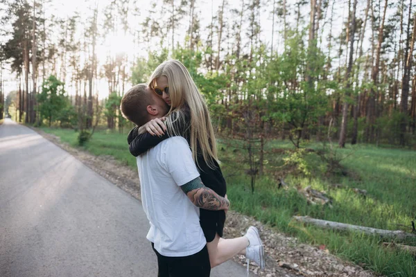 Tatuado Homem Segurando Menina Loira Midair Estrada Floresta — Fotografia de Stock