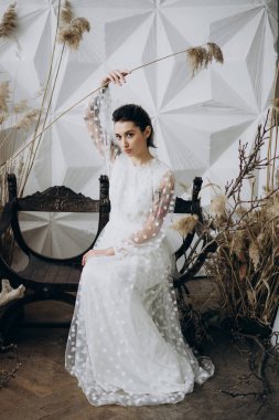 beyaz elbiseli neşeli kadın ahşap bankta oturan ve elinde kurutulmuş çim tutarak 