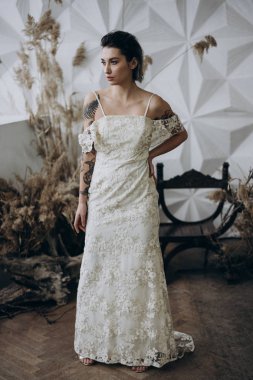  brunette in vintage white dress standing around studio decorations  and looking away 