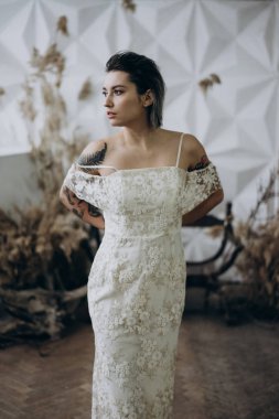 boho tarzında beyaz elbise giyen ve uzağa bakan dövmeli bayan portresi