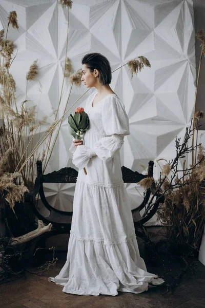 side view of woman holding exotic flower in the hands wearing white dress