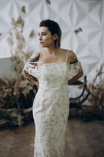 boho tarzında beyaz elbise giyen ve uzağa bakan dövmeli bayan portresi