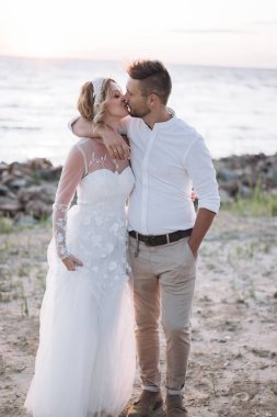 gün batımında sahilde öpüşen genç kadın ve adam 