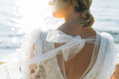 gün batımında sahilde duran şık gelinin arka görünümü 