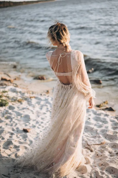 back view of woman in long dress standing on the sandy beach