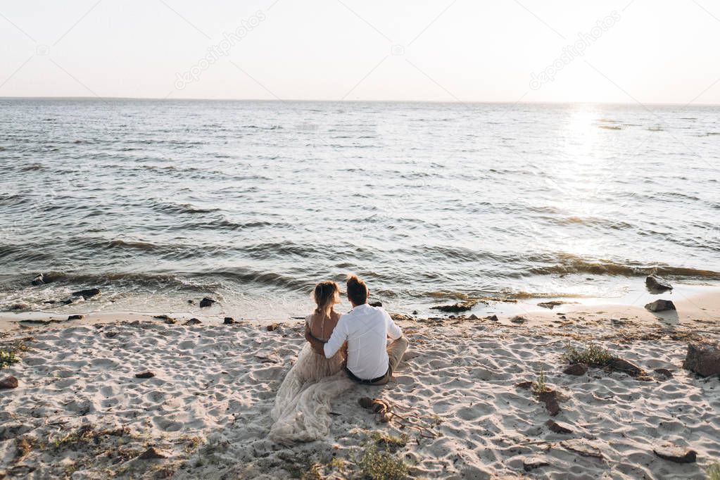 back view of couple sitting on the beach at the sunset 