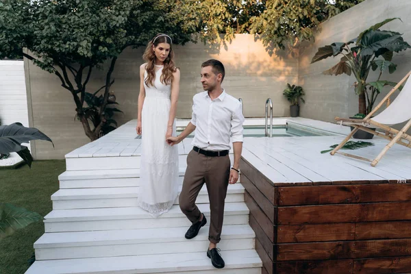 arka planda yüzme havuzu ile bahçede yürüyen şık erkek ve kadın, Tam Uzunlukta atış 