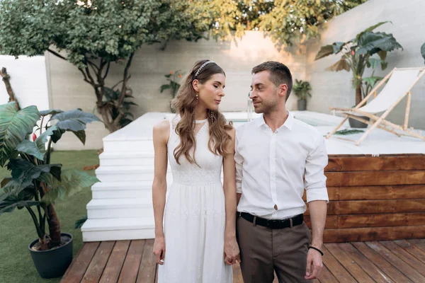 arka planda yüzme havuzu ile bahçede duran genç adam ve kadın