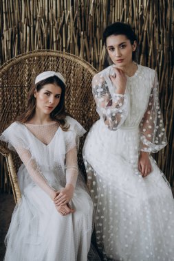  beyaz elbiseli genç kadınlar büyük sandalyede oturur ken kameraya bakıyor 