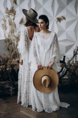 beyaz elbiseler ve fedora şapka giyen iki şık kadın arka arkaya ayakta stüdyoda poz