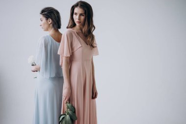 renkli elbiseler giyen iki genç kadın hafif arka planda arka arkaya ayakta ve elinde çiçekler tutarak, stüdyo çekim 