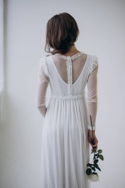 Hafif arka planda kadının arka görünümü ve elinde gül çiçeği tutarak 