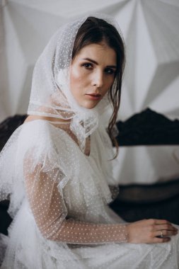  stüdyoda ahşap bankta oturan kameraya bakarak kafasına şık şal giyen bayan 