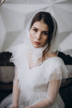  stüdyoda ahşap bankta oturan kameraya bakarak kafasına şık şal giyen bayan 