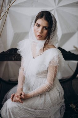  stüdyoda ahşap bankta oturan kameraya bakarak kafasına şık şal giyen bayan 