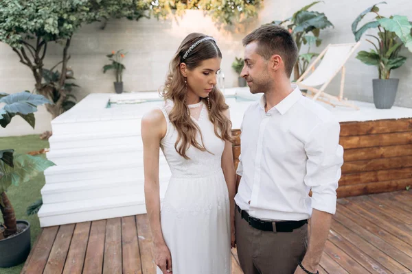 arka planda yüzme havuzu ile bahçede duran genç adam ve kadın