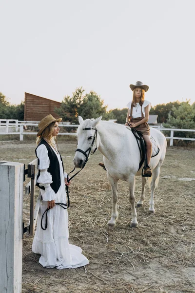 woman holding bridle with girl sitting on white horse