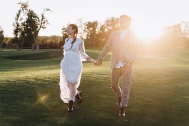 yakışıklı adam el ele tutuşan ve batan güneşe karşı yeşil çim yürüme ile beyaz elbiseli güzel hamile kadın