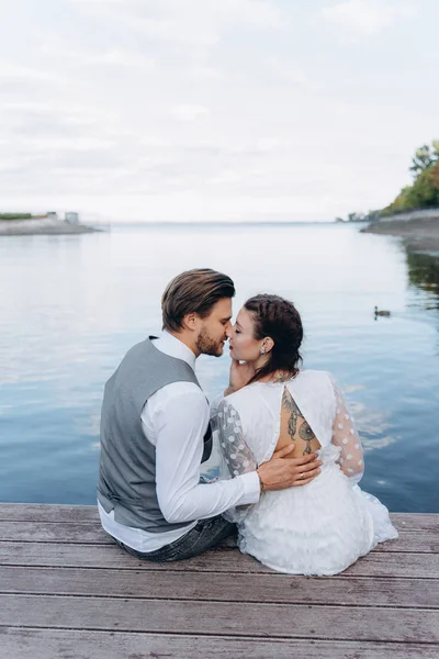 背景美丽的夫妇接吻和坐在对湖的木制码头 — 图库照片