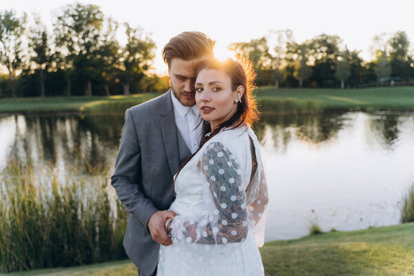 красивая беременная женщина в белом платье с красивым мужчиной, идущим по зеленой лужайке против заходящего солнца
