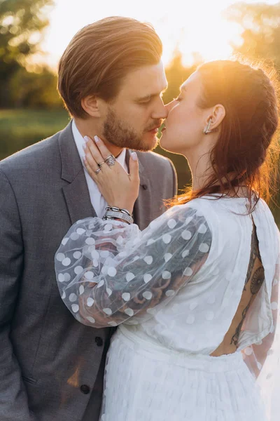 美丽的孕妇在白色礼服与英俊的男人亲吻在绿色草坪对夕阳 — 图库照片