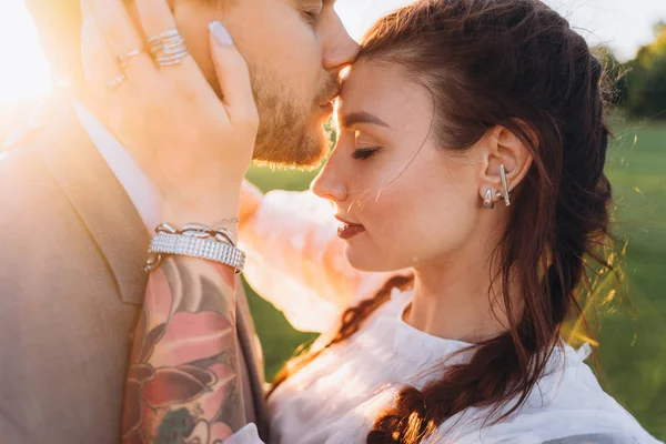 handsome man kissing woman\'s forehead against the setting sun